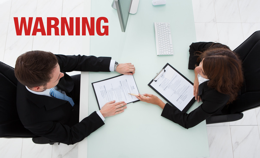 photo of two people during a job interview with a warning label superimposed over the resume that is being reviewed
