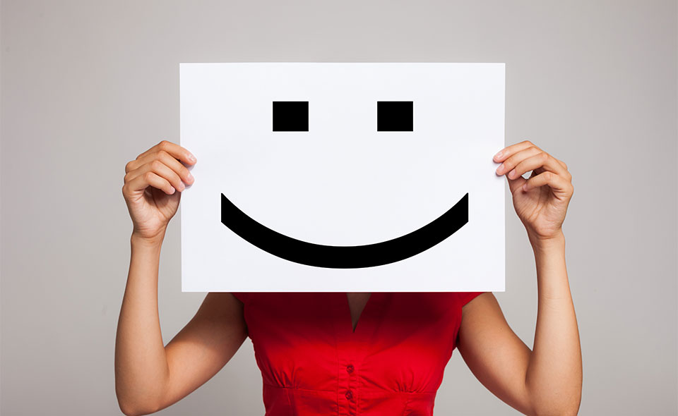 Picture of a woman holding up a smiley face in front of her head.