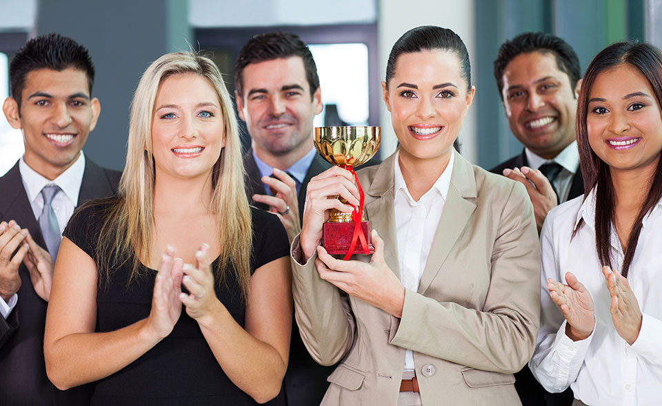 A group of workers who have been shown employee appreciation as shown by the trophy they are celebrating.